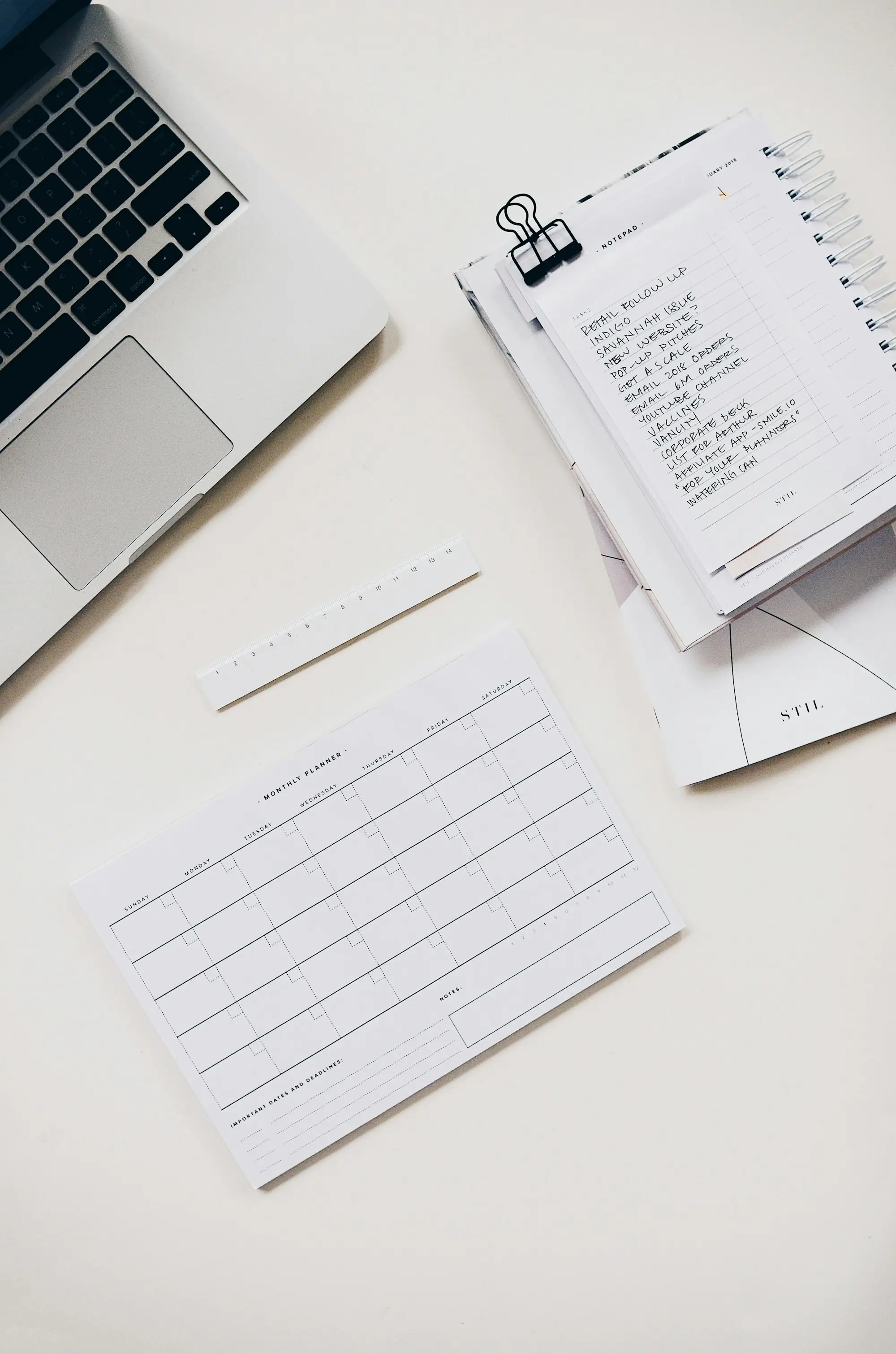 A laptop beside neatly arranged paperwork, a binder-clipped notebook and printed forms on a clean desk.