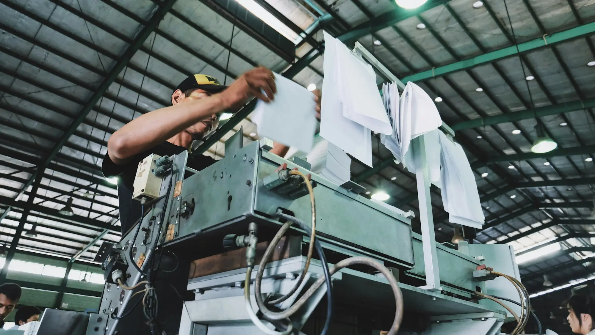 Print shop operator loading paper stock into an industrial press during a customer order run